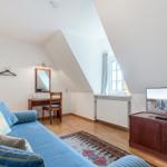 A bedroom with sloped ceiling, sofa, desk, and TV.