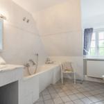 Bathroom with bathtub, sink, and toilet. Window with curtains and radiator.
