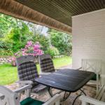 Patio with table and chairs, view of green garden with pink flowers.
