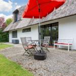 House with thatched roof and garden area with table, chairs, and umbrella.