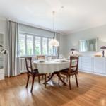 Dining room with wooden floor, table and chairs, windows and mirror on the wall.