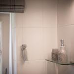 Bathroom with window, white tiles, and glass shelf with care products.