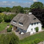 Cottage with thatched roof, garden, and terrace. Surrounded by trees and greenery.