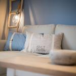 Sofa with cushions and wooden table. Background: wall and lamp.