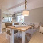 Dining area with wooden table, bench seating, and kitchen area in background.