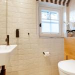 Badezimmer mit Waschbecken, Toilette und Fenster mit Jalousie.