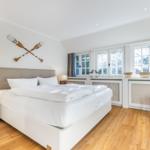 Schlafzimmer mit Bett, Nachttisch, Stuhl und Fenstern.