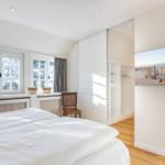 Schlafzimmer mit Bett, Fenster, Kleiderschrank und Wandbild.