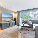Ein Wohnzimmer mit grauem Sofa, runden Tischen und großem Fenster.