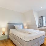 Schlafzimmer mit Doppelbett, Nachttisch und Fenster mit Vorhängen.