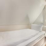 Ein Schlafzimmer mit weißem Bett, Spiegel und Lampe an der Wand.
