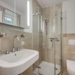 Bathroom with shower, sink, and toilet. Lit mirror cabinet.