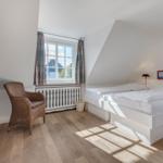 Bedroom with white bed, wooden floor, and window with curtains.