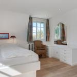 Bedroom with white bed, window, mirror and chair.