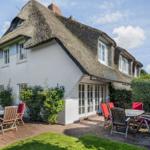 White villa with thatched roof and terrace with tables and chairs.