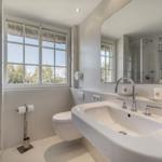 Bathroom with sink, toilet, and shower. Window with view of trees.