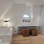 Bedroom with sloped ceiling, bed, lamp, window, and two baskets.