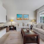 Living room with fireplace, two sofas, and glass-top table. Windows show garden.