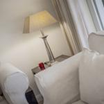 A white armchair next to a nightstand with lamp and red glass.