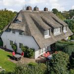House with thatched roof, garden and red chairs
