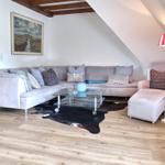 Wohnzimmer mit Sofa, Couchtisch und Stehlampe unter Dachschräge.