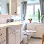 Badezimmer mit Waschbecken, Toilette und Fenster mit Vorhängen.