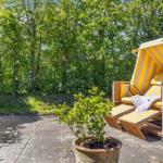 Helle Strandkörbe auf Terrasse mit Pflanze und Bäumen im Hintergrund.
