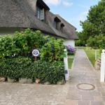 Steinweg führt zu einem Haus mit Strohdach und grüner Hecke.