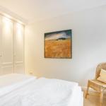 Bedroom with bed, wardrobe, and chair with cushion.