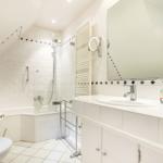 Bathroom with shower, sink, and toilet. White tiles and mirror.