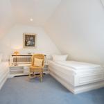 Room with two beds, chair, and window. Wall picture and lamp visible.