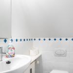 Bathroom with sink, mirror, and toilet. Walls tiled with blue accents.