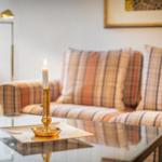 A glass table with a candle and brass holder in front of a sofa with checkered upholstery.