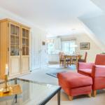Living room with red armchairs, glass table, and wooden cabinet. Kitchen and dining area in background.