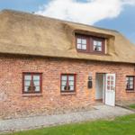 Haus mit strohgedecktem Dach und rotem Backsteinmauerwerk. Weiße Tür und Fenster mit weißen Vorhängen.