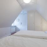 Schlafzimmer mit Dachschrägen, weißem Bett und Kleiderschrank.