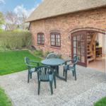 Roter Backsteinbau mit strohgedecktem Dach und Gartenbereich mit Tisch und Stühlen.