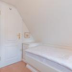 Ein Schlafzimmer mit weißem Bett und Tür unter Dachschrägen.