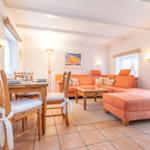 Wohn- und Essbereich mit orangefarbenem Sofa, Holztisch und Stühlen mit weißen Sitzkissen.
