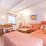 Wohn- und Essbereich mit orangefarbenem Sofa, Holztisch und Fenstern.