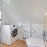 Badezimmer mit Waschmaschine, Toilette und Dusche unter Dach