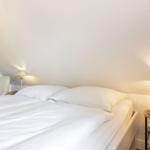 Schlafzimmer mit Doppelbett, zwei Nachttischen und Lampen an der schrägen Wand.