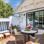 Terrasse mit Rattanmöbeln, Strandkorb und Blumen vor einem Haus mit Strohdach.