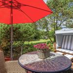 Terrasse mit rotem Sonnenschirm, runden Tisch und Strandkorb.