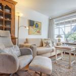 Wohnzimmer mit Sofa, Sessel und Holzschrank. Fenster mit Blick auf Dächer.