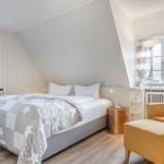 Bedroom with bed, armchair, and two windows.