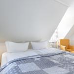 Bedroom with sloped ceiling, bed with gray coverlet, and yellow seating area.