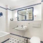 Bathroom with bathtub, sink, and toilet. Blue tile trim and mirror.