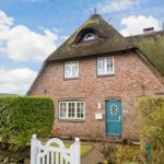 House with thatched roof, green door, and hedges. Number 24a.