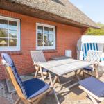 Terrace with table, chairs, and beach chair in front of red brick house with thatched roof.